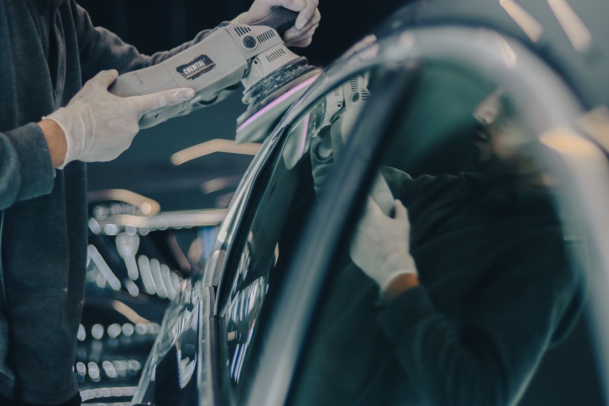 Profissional polindo a pintura de um carro, com reflexos das luzes da oficina