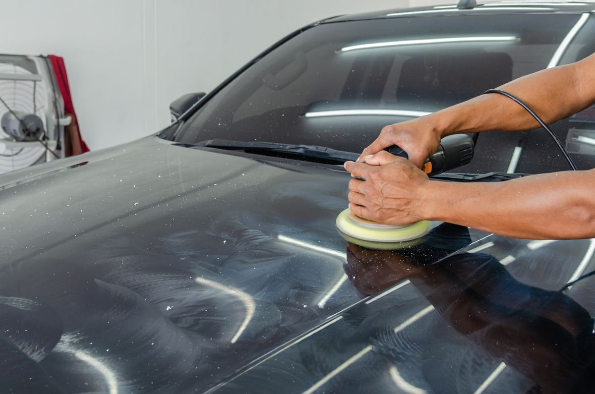 Mãos de um profissional realizando o polimento do capô de um carro preto